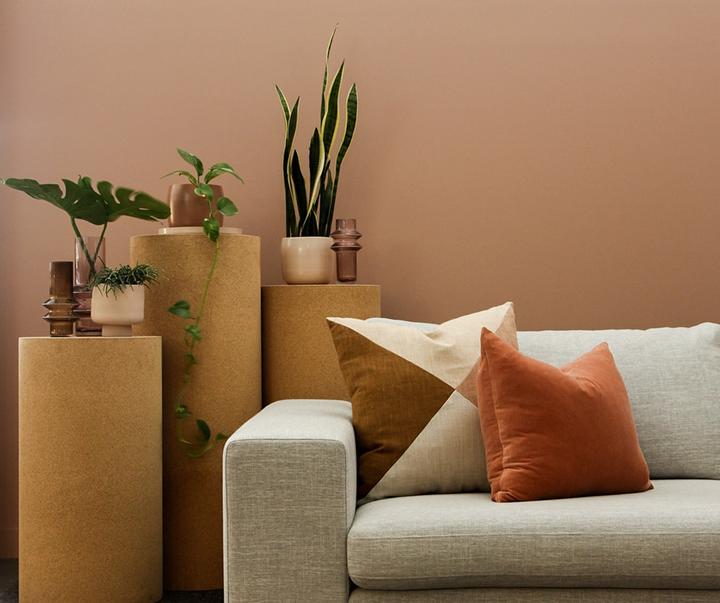 A cozy corner with a light sofa, orange pillows, and potted plants on wooden cylinders.