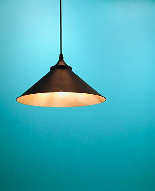 Dark bronze cone-shaped pendant lamp hanging against a turquoise wall.